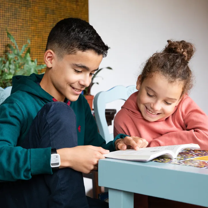 A child wearing the Syde device on the wrist reading a book with his sibling